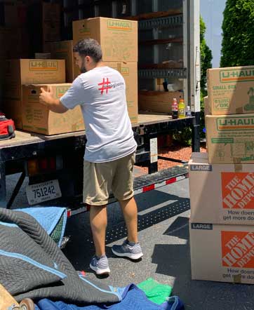 BG Home Movers Moving Man loading boxes into the moving truck with lots of boxes sitting in the driveway.